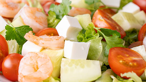 A salad with shrimp, tomatoes, cucumbers, and lettuce
