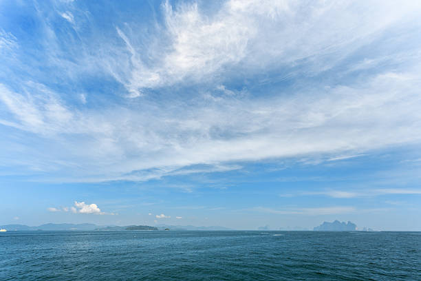 Bright blue sky and light clouds above calm sea with distant islands visible on the horizon.