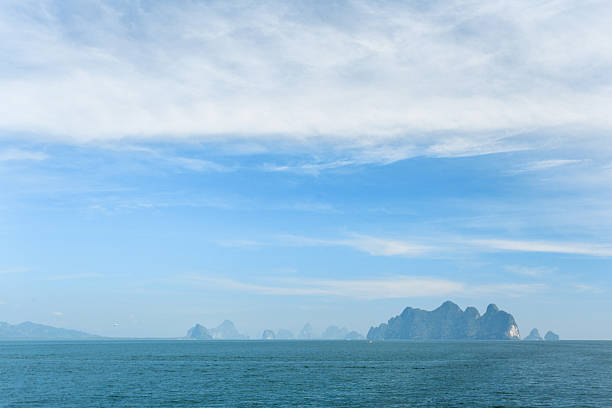 Tranquil Thailand: calm sea, blue sky, soft clouds, and distant islands.
