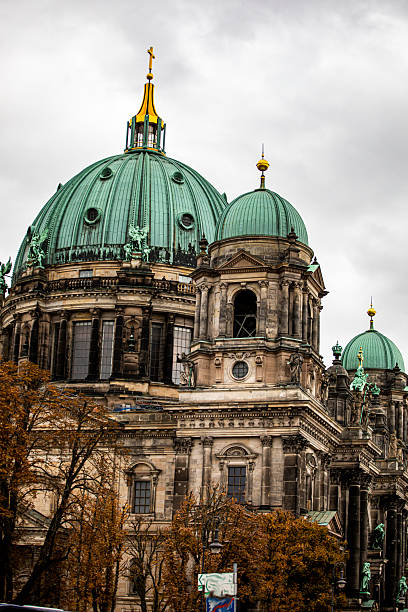 A view of the Berlin Cathedral's green dome and the historic bridge over the River Spree in Berlin, Germany, under a clear blue sky. The scene captures the essence of Berlin's architectural heritage.