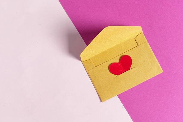A handmade yellow envelope with a red heart sits on a pink and white background for gifts.