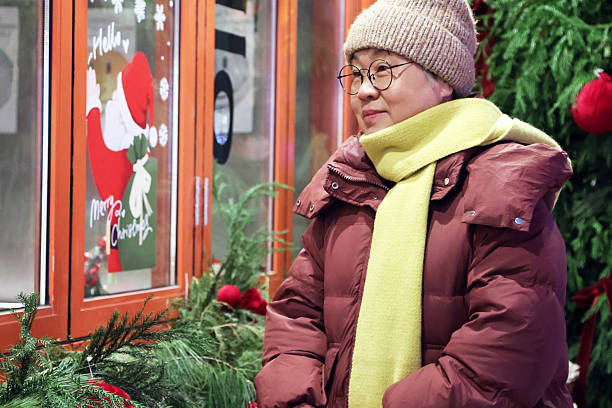 An elderly Asian woman sits next to the Christmas tree.