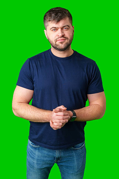 istock Man standing with a thoughtful expression in a casual outfit against a green background 2250905098