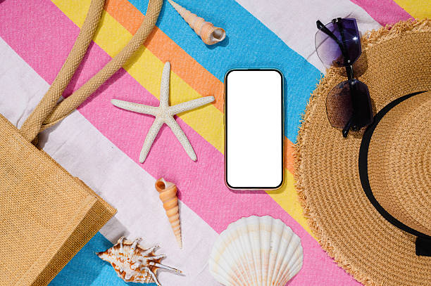 istock A smartphone with a white screen on the beach. A phone with a blank screen on a beach mat with shells. Sea travel advertising concept. 2250905115