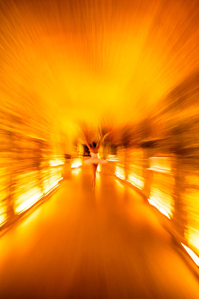 A dreamy, abstract motion-blur photograph of a ballet dancer performing in a warm, golden-lit underground space. The dynamic zoom effect creates a sense of energy, fluid movement and artistic expression. Ideal for themes of creativity, performing arts, dance, motion, and atmospheric interiors.