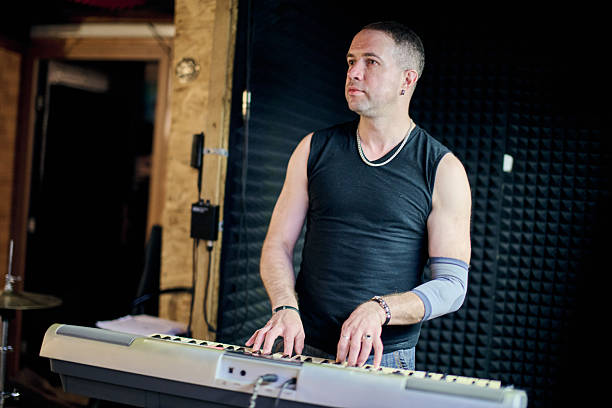 Adult male with short hair, plays keyboard in acoustic room. Padded walls for sound absorption create focused atmosphere. Soft light highlights musicians concentration