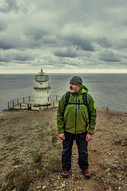 istock Explorer stands on coastal cliff near old lighthouse overlooking stormy sea under cloudy sky 2250917897