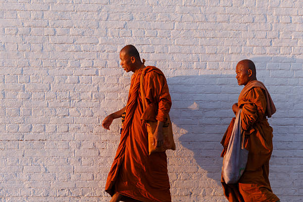 Two Buddhist monks walking along a white brick wall in warm evening light in Lumbini, Nepal.