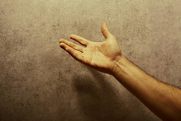 Male hand raised in front of a gray wall pleading