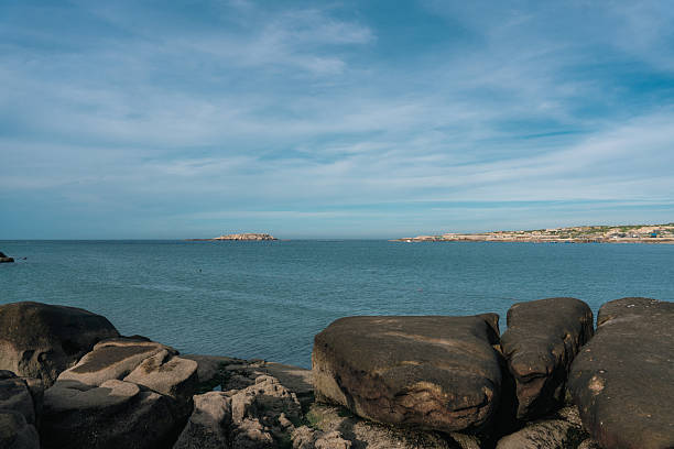 A picturesque coastal scene featuring rocks, calm sea, and clear sky, showcasing natural beauty.