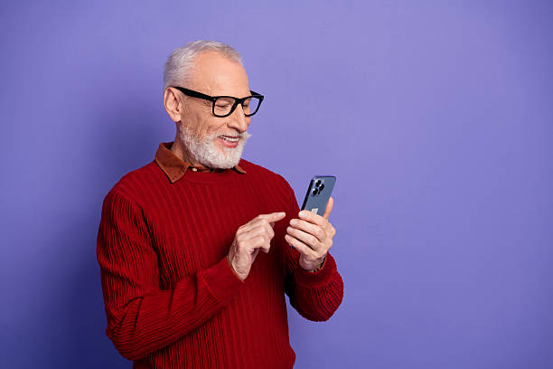 istock Elderly man in red sweater using smartphone against purple background smiling and enjoying technology 2250924630