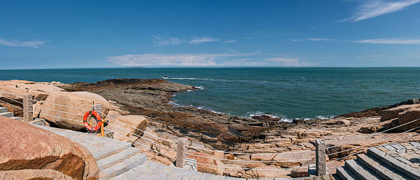 A picturesque coastal scene featuring a rocky shoreline and the vast clear blue sea under a bright sky.