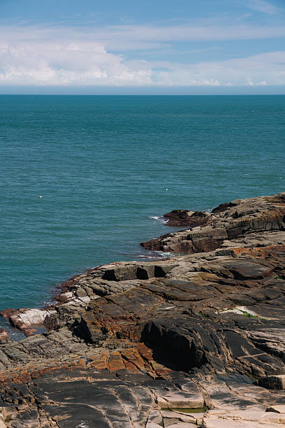 A picturesque coastal scene featuring a rocky shore and clear blue sea under a partly cloudy sky.