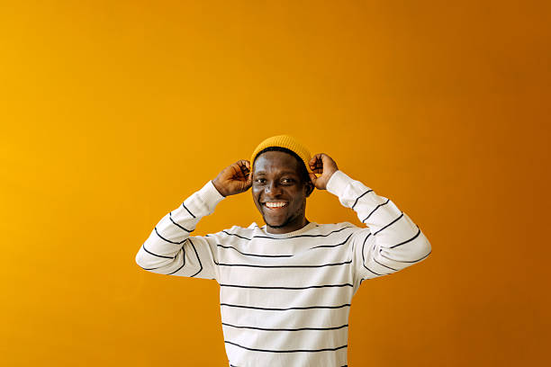 istock Young black man smiles while wearing a yellow beanie in a studio with a bright yellow background 2250925531