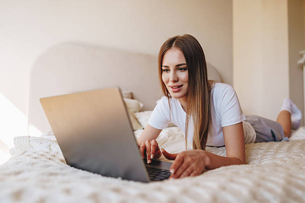 istock Young woman using laptop while lying on bed in cozy bedroom during the day 2250925613