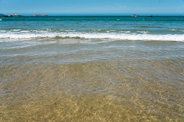 The image shows clear blue sea water with gentle waves rolling onto a sandy shore, creating a serene coastal scene.
