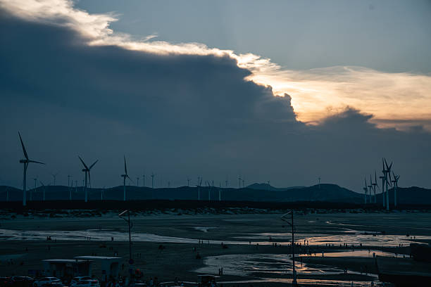 A beautiful sunset scene featuring wind turbines under a sky with dark clouds and glowing light.