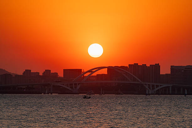 Sunset silhouette of Wuyuan Bridge in Xiamen, China, captured with a telephoto lens, showing the enormous sun.
