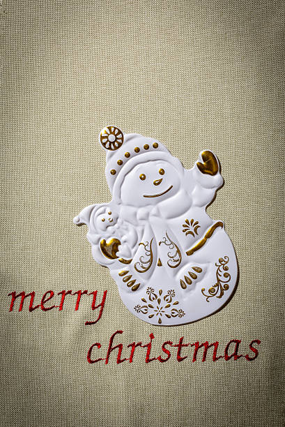 A snowman figure is placed on fabric with a Merry Christmas greeting. The snowman has details like a hat, buttons, and patterns.