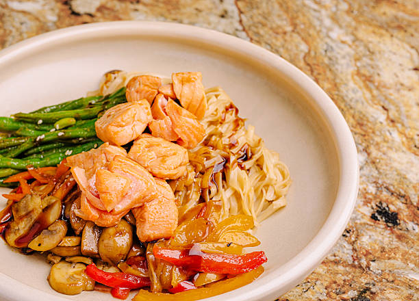 Delicious salmon bowl with vegetables and noodles on a marble surface