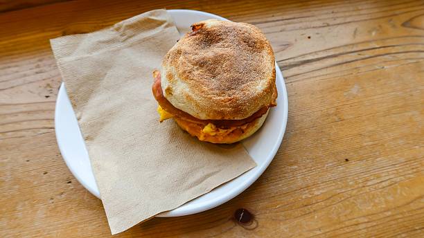 close up of ham, cheese and egg muffin with tissue on a plate placed on the wooden table