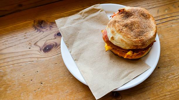 close up of ham, cheese and egg muffin with tissue on a plate placed on the wooden table