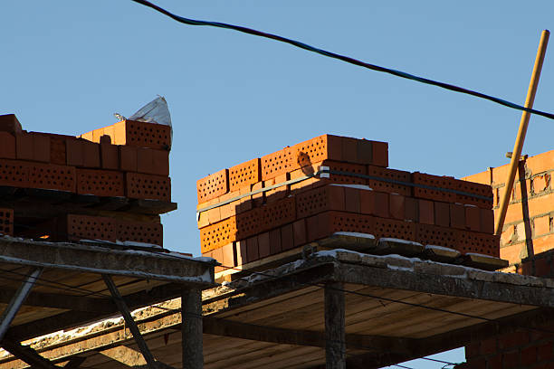 a stack of new, perforated red clay bricks resting on the unfinished upper level of a building under construction
