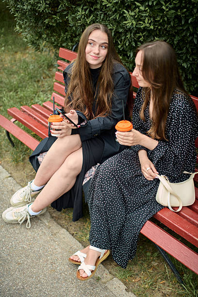 istock Young girlfriends sharing coffee and gossip on Red Park bench 2250942600
