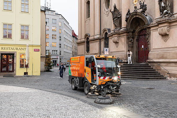 Prague, czech republic - december 2, 2025: electric orange street sweeper cleaning a historical square in prague with buildings in background