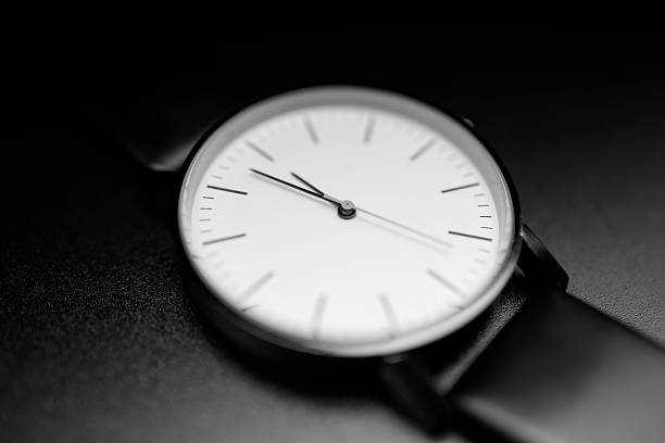 A close-up black-and-white image of a sleek wristwatch resting on a dark surface. The minimal dial and crisp lines evoke timeless elegance and modern sophistication for fashion, lifestyle, or branding uses.