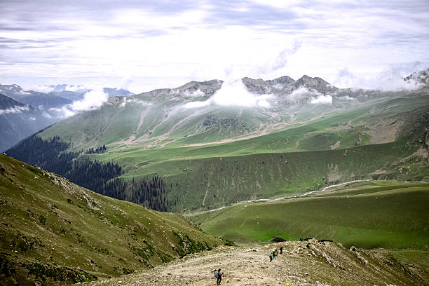 A panoramic Himalayan green valley with rolling hills, drifting clouds, and trekkers on a scenic trail. Perfect for themes of adventure, nature, travel, hiking, and outdoor exploration.