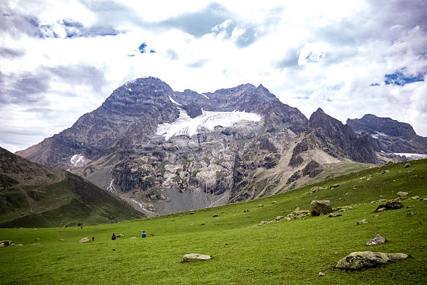 A panoramic Himalayan green valley with rolling hills, drifting clouds, and trekkers on a scenic trail. Perfect for themes of adventure, nature, travel, hiking, and outdoor exploration.