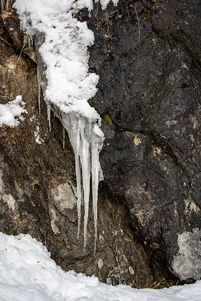Icicles hang off eavestrough in sunlight and lofty clouds in sky