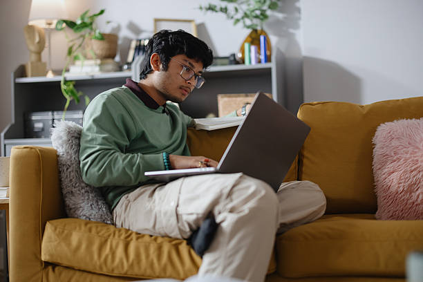 istock Indian Male Student Studying Remotely from Home Using Laptop on Sofa 2250953684