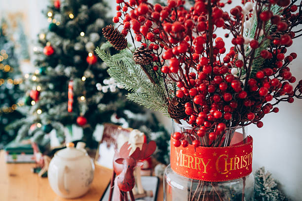istock Decorations for Christmas with red berries and green branches placed on a table near a Christmas tree and other festive items 2250956880