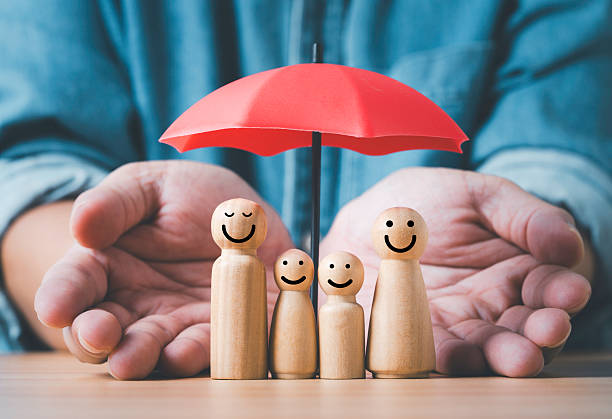 istock Wooden family figures under a protective umbrella with caring hands symbolizing life insurance safety security, and support for representing healthcare assurance and wellness in a warm family concept. 2250959697