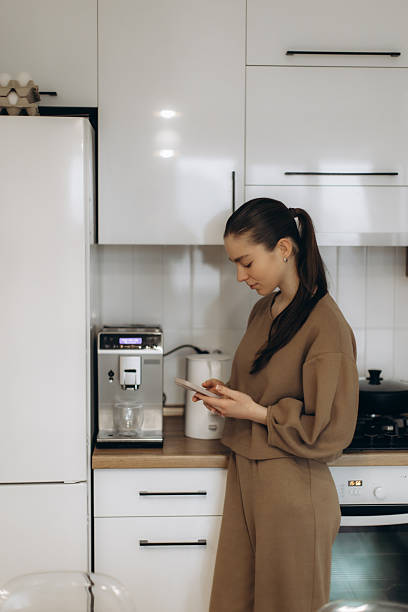istock Woman Using Smartphone in Modern Kitchen With Coffee Machine and Appliances 2250961247