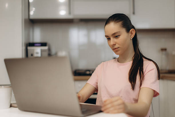 istock Young Woman Focused on Work Using a Laptop in a Modern Kitchen 2250961261