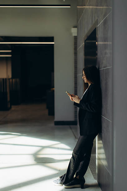 istock Professional Woman Using Smartphone Leaning Against Wall in Modern Office Space 2250968341