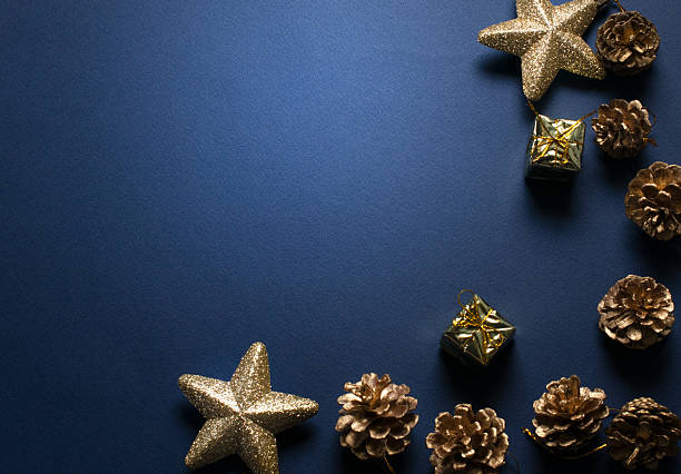 Christmas minimalistic dark blue background with decorative glittering stars, golden gift box and cones for tree decoraton. New Year winter holiday composition with decor and space for text, top view.