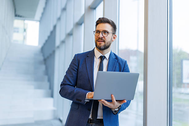 istock Businessman standing in office looking out a window holding laptop 2250973037
