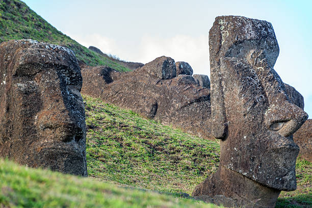 Multiple moai statues stand along the grassy slopes of the Rano Raraku quarry, the volcanic site where the sculptures were carved on Easter Island, Rapa Nui, Chile.
