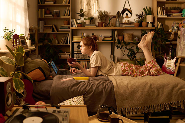 istock Young Woman Lying on Bed Using Laptop and Eating Breakfast 2250974395