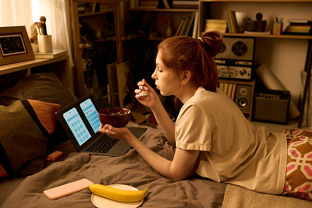 istock Young Woman Eating Breakfast While Using Laptop in Bedroom 2250974805
