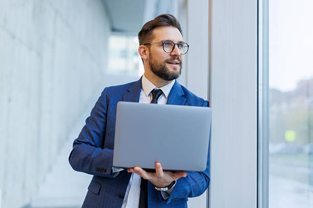 istock Businessman holding laptop, looking out window 2250977105