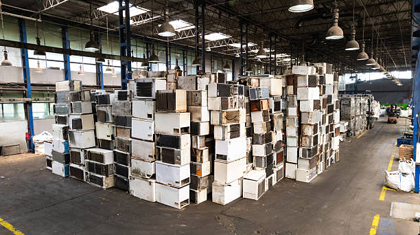 Recycling warehouse where skilled worker operating forklift near piles of electronic scrap and machinery