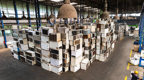 Recycling warehouse where skilled worker operating forklift near piles of electronic scrap and machinery