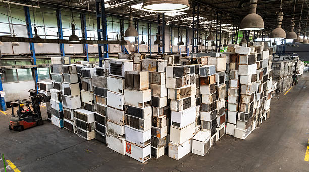 Recycling warehouse where skilled worker operating forklift near piles of electronic scrap and machinery
