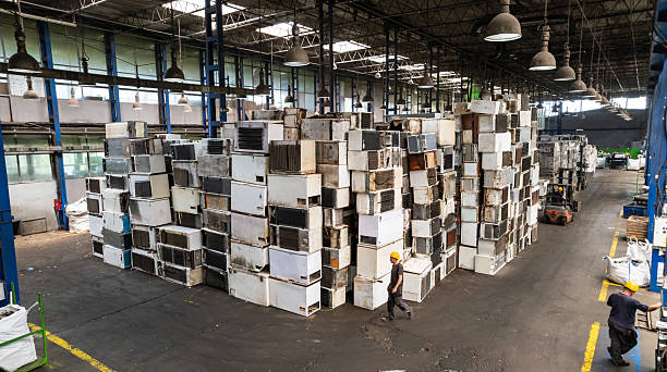 Recycling warehouse where skilled worker operating forklift near piles of electronic scrap and machinery