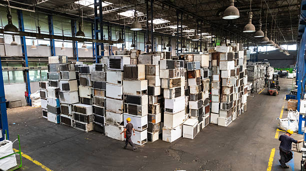 Recycling warehouse where skilled worker operating forklift near piles of electronic scrap and machinery